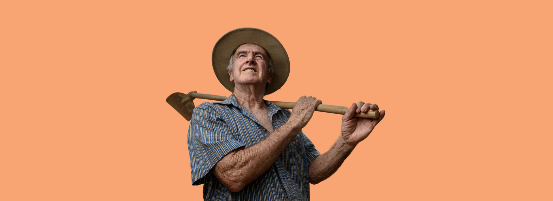 Agricultor com chapéu de palha olha para cima enquanto apoia sua enxada no ombro